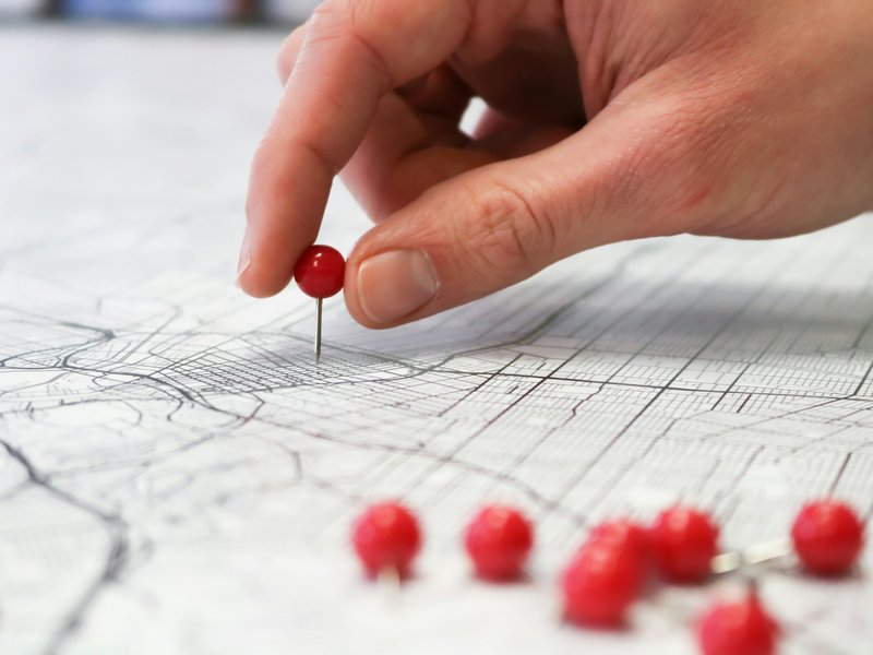 Hand placing red push pins on a map